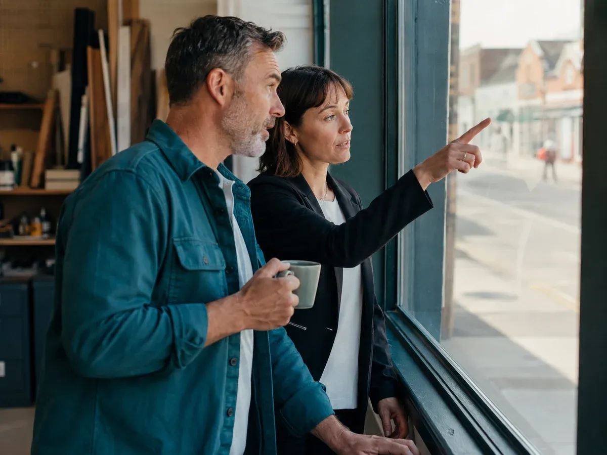 Business owner and adviser discussing their local market by a workshop window